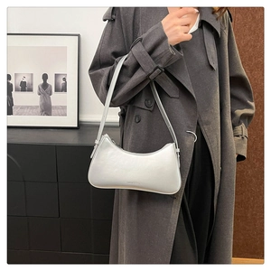 Detail of silver metallic crescent bag with adjustable strap on gray trench coat