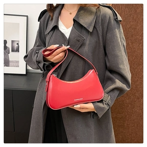 Detail of red crescent leather shoulder bag with white text held by model in trench coat