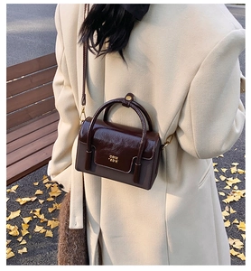 Detail of a shiny dark brown leather crossbody bag with golden logo in autumn setting