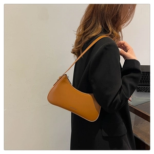 Close-up of caramel faux leather baguette bag worn by model in professional attire