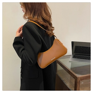 Detail view of a caramel leather half-moon shoulder bag with a fashion text logo
