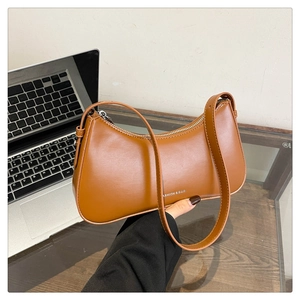 Detailed close-up of brown PU leather baguette bag with silver zipper and printed text