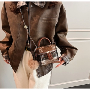 Detail van de bruin geblokte wollen crossbody tas met pluche textuur en decoratieve pompon
