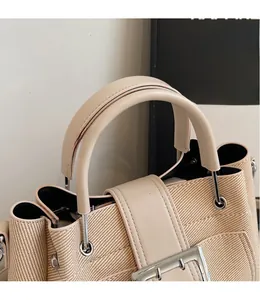 Detail of beige woven bucket bag with smooth leather trim and silver metal buckle