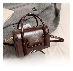 Detail of dark brown retro square bag showing shiny leather texture and golden metal logo