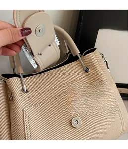 Macro detail of beige textured fabric bucket bag with smooth leather trim and silver magnetic clasp