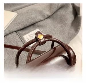 Close-up of the glossy leather handle with gold snap button on a dark brown handbag