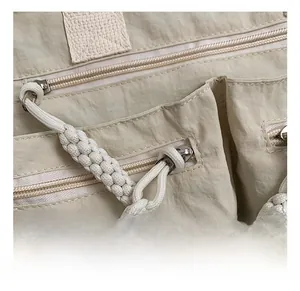 Detail of beige nylon crossbody bag showing silver hardware and woven rope zipper pulls