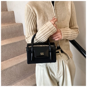 Detail of black glossy handbag with gold hardware and COIH '2DN logo on stairs