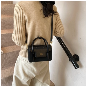 Detail of black mini square bag featuring glossy patent leather and gold clasp buckle