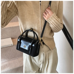 Detail of black patent leather crossbody bag with gold logo on beige knit outfit