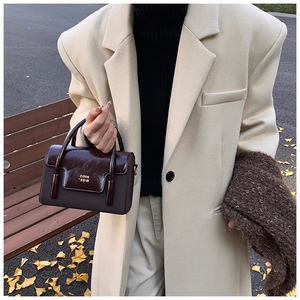 Close-up of retro square handbag in glossy brown leather styled with an autumn coat