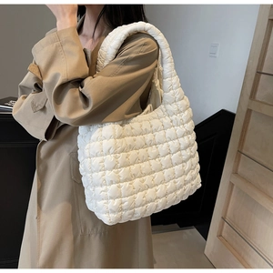 Close-up of white quilted puffer tote bag on shoulder with khaki trench coat
