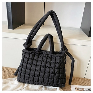 Detailed view of the black quilted puffer bag with unique knotted strap on straw mat
