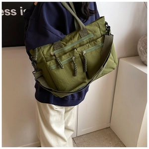 Detail of army green nylon multi-pocket tote bag with woven zipper pulls and wide strap