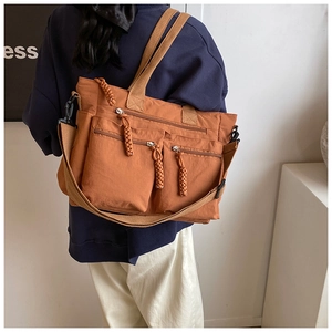 Detail of burnt orange nylon tote bag showing multiple pockets and adjustable canvas strap
