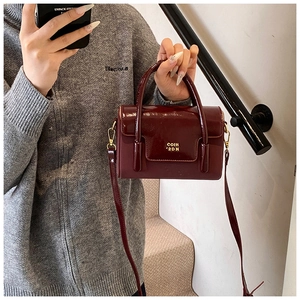 Detail of glossy wine red square bag with gold COIH '2DN lettering and crossbody strap