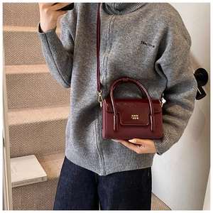 Detail of burgundy leather satchel with gold lettering and metallic crossbody hooks