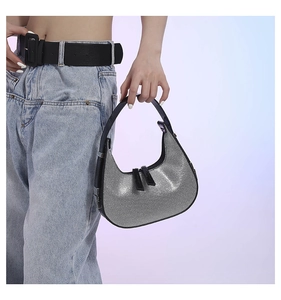 Detail of silver glitter crescent bag featuring dual zippers and black leather handles