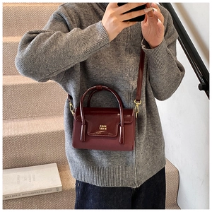 Detail of burgundy leather handbag with metallic logo and textured flap on model