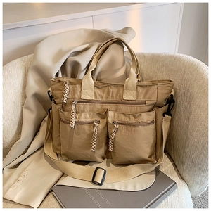 Detail of khaki nylon tote bag featuring multi-pocket design and woven zipper charms