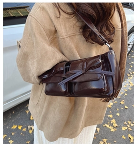 Detail of a dark brown glossy patent leather shoulder bag with decorative bow pockets