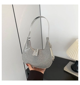 Close-up of sparkling silver rhinestone crescent shoulder bag held by hand in luxury setting
