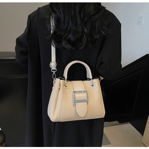 Detail of beige bucket bag with silver buckle worn over a black blazer for contrast