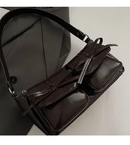 Detail der dunkelbraunen glänzenden PU-Ledertasche mit zwei Vordertaschen und Schleifen