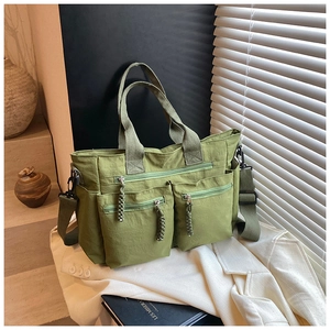 Detailed view of green nylon tote bag with multiple zipper pockets and woven rope pullers