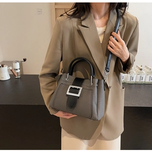 Detail view of grey textured bucket bag with black leather handles and silver buckle