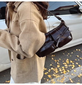 Detail of dark brown glossy PU bag with bow ribbon and multiple pockets in autumn setting