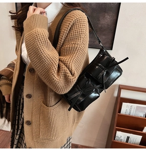 Detail of glossy black PU shoulder bag featuring dual front pockets and leather bow decoration