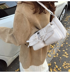 Detail of white PU shoulder bag with decorative bows and double pockets in autumn setting