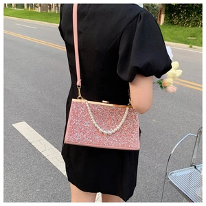 Detail van roze pailletten clutch met parelketting en gouden frame op zwarte jurk