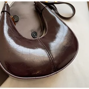 Detail of dark brown crescent bag showing pleated glossy patent leather and metal zipper
