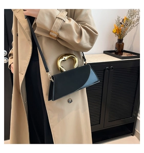 Detail of elegant black leather square bag featuring a sculptural gold wavy handle