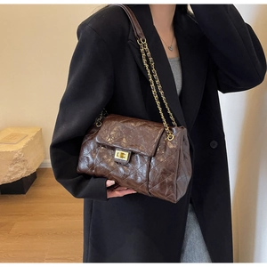Detail of dark brown quilted crossbody bag featuring a golden metallic twist lock closure