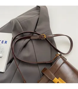 Détail de la bandoulière réglable en cuir et ferrures dorées sur le sac seau marron