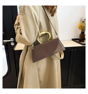 Detail of a brown leather square handbag featuring a unique gold U-shaped metal handle