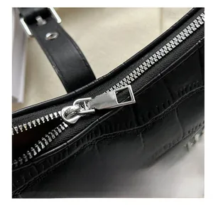 Close-up of smooth silver metal zipper and crocodile texture on black shoulder bag