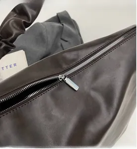 Detail of premium brown leather bucket bag showing smooth silver zipper and pleated handle