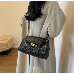 Macro detail of black quilted texture with gold chain strap and metal turn-lock closure