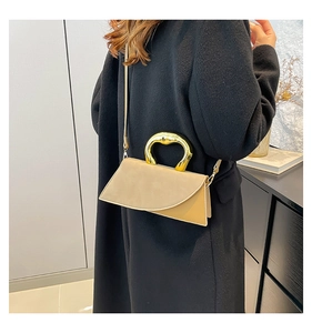 Detail of light brown crossbody bag with unique artistic gold metal handle on model