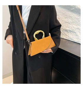 Close-up of a tan leather crossbody bag with a circular gold metal handle on a black coat
