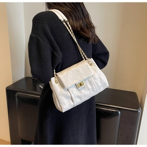 Detail of white quilted crossbody bag with gold chain strap and turn-lock closure