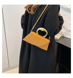 Asymmetric ginger leather square bag with gold U-shaped handle shown on a black wool coat