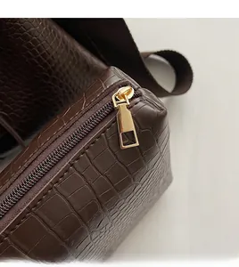 Detail of smooth gold zipper on brown crocodile-embossed bucket bag with nylon strap