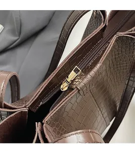 Close-up of smooth gold zipper and crocodile embossed texture on a dark brown bucket bag