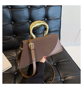 Detail view of brown asymmetric handbag with large gold circular metal handle on leather seat